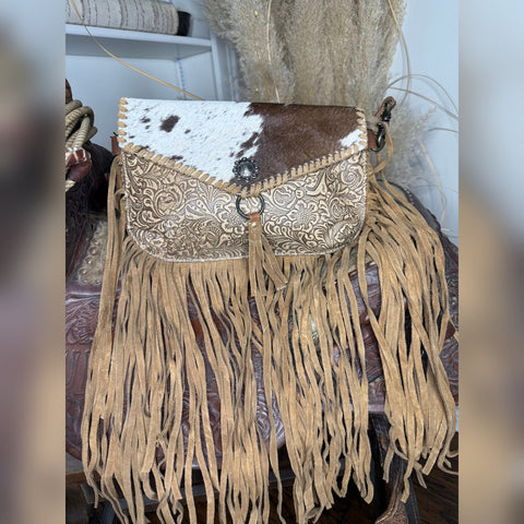 Western crossbody with a brown and white cowhide flap, cream tooled leather body and fringe down the sides and bottom