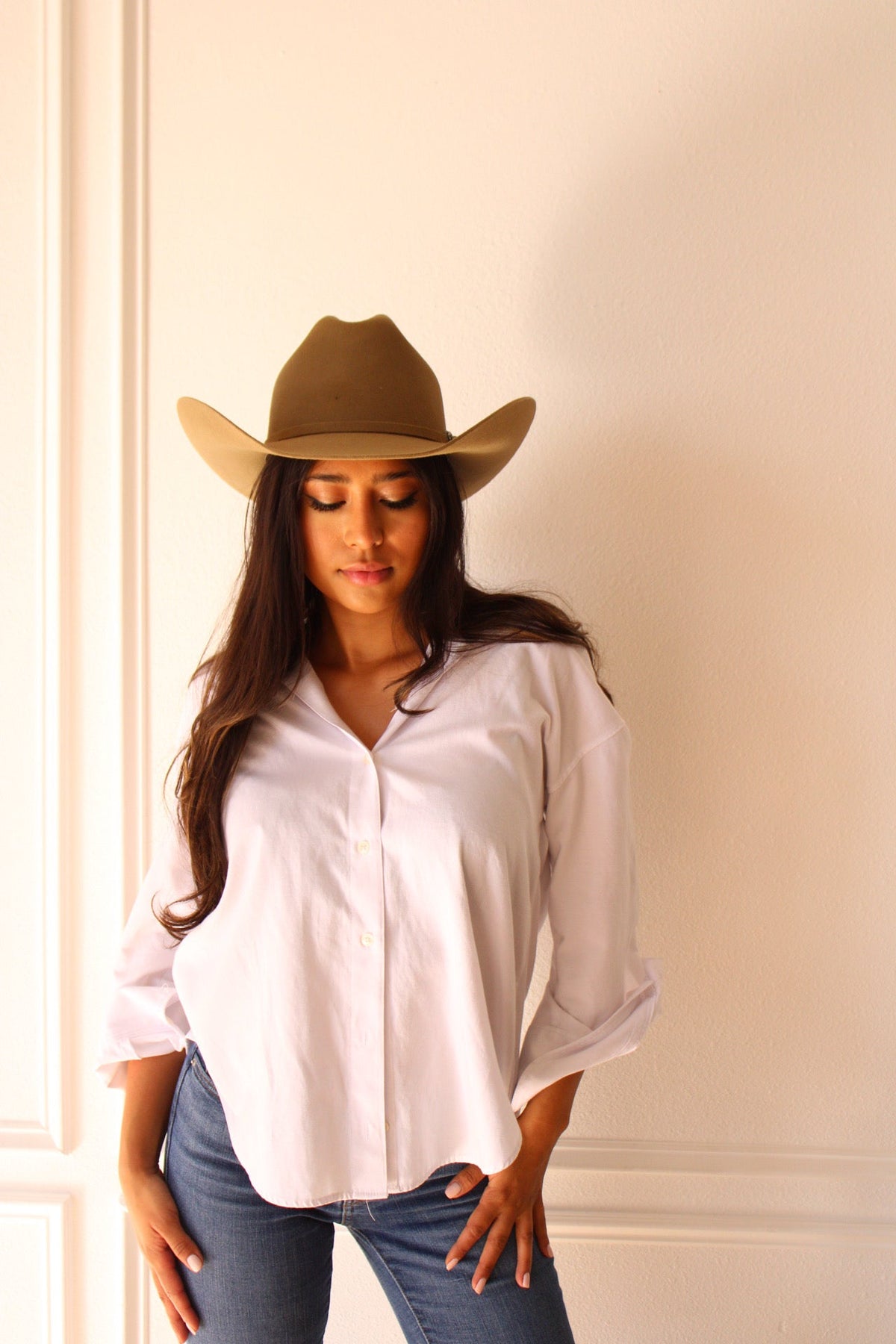 Model in a white shirt and jeans wearing the camel Wren merino wool cowboy hat, eyes down