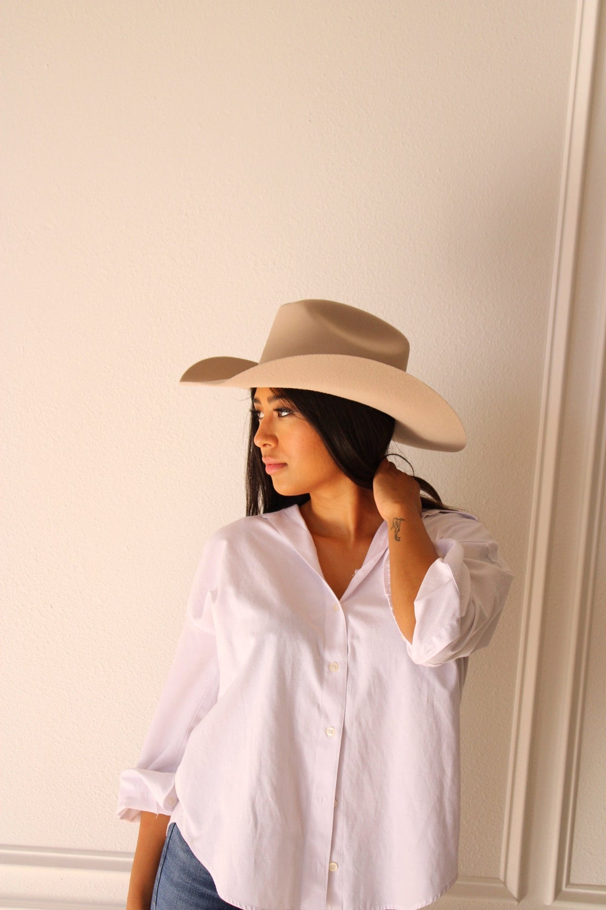 Model in a white shirt wearing the desert sand Wren merino wool cowboy hat, looking over her shoulder