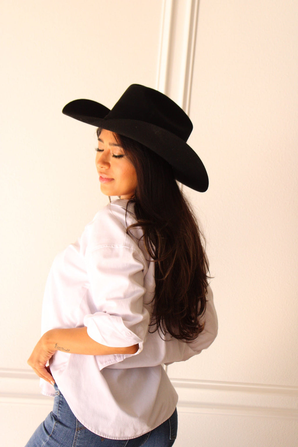 Model in a white shirt and jeans wearing the black Wren merino wool cowboy hat, head tilted down