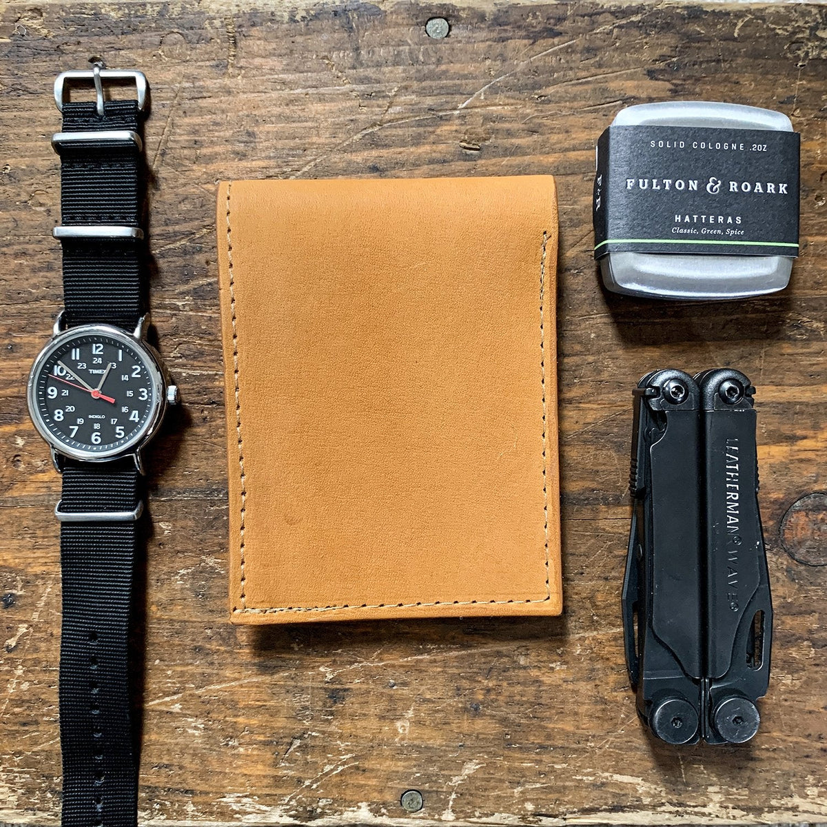 Tan baseball glove leather wallet on a wood bench beside a watch and a multi-tool