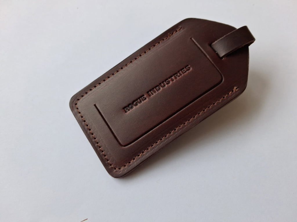 Dark brown leather luggage tag with the Rogue Industries mark debossed on the front panel