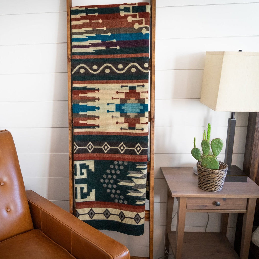 Forest green, rust and cream Andean alpaca blend blanket hanging on a wooden ladder beside a leather chair