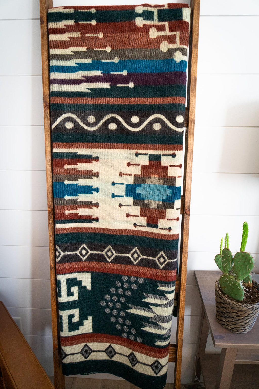 Full length of the Evergreen Andean alpaca blend blanket on a blanket ladder beside a potted cactus
