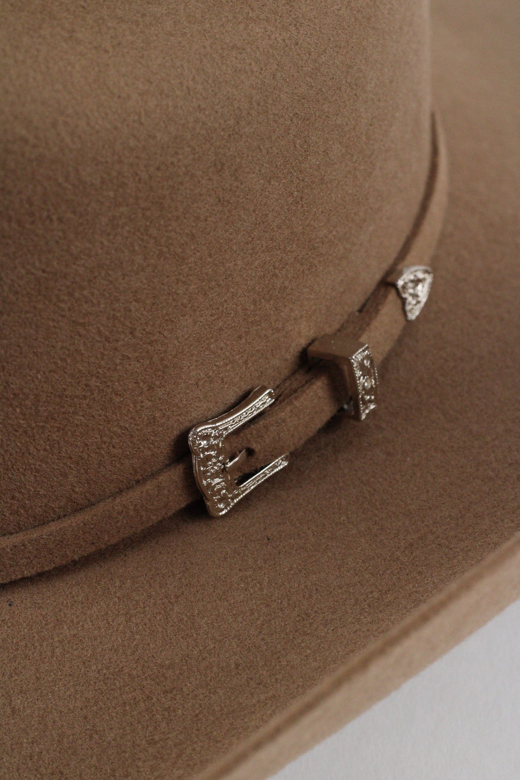 Close view of the matching band and engraved silver-tone buckle set on the camel Wren cowboy hat