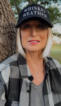 Woman wearing a black Whiskey Weather trucker hat with white embroidered lettering