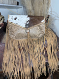 Western crossbody with a brown and white cowhide flap, cream tooled leather body and fringe down the sides and bottom