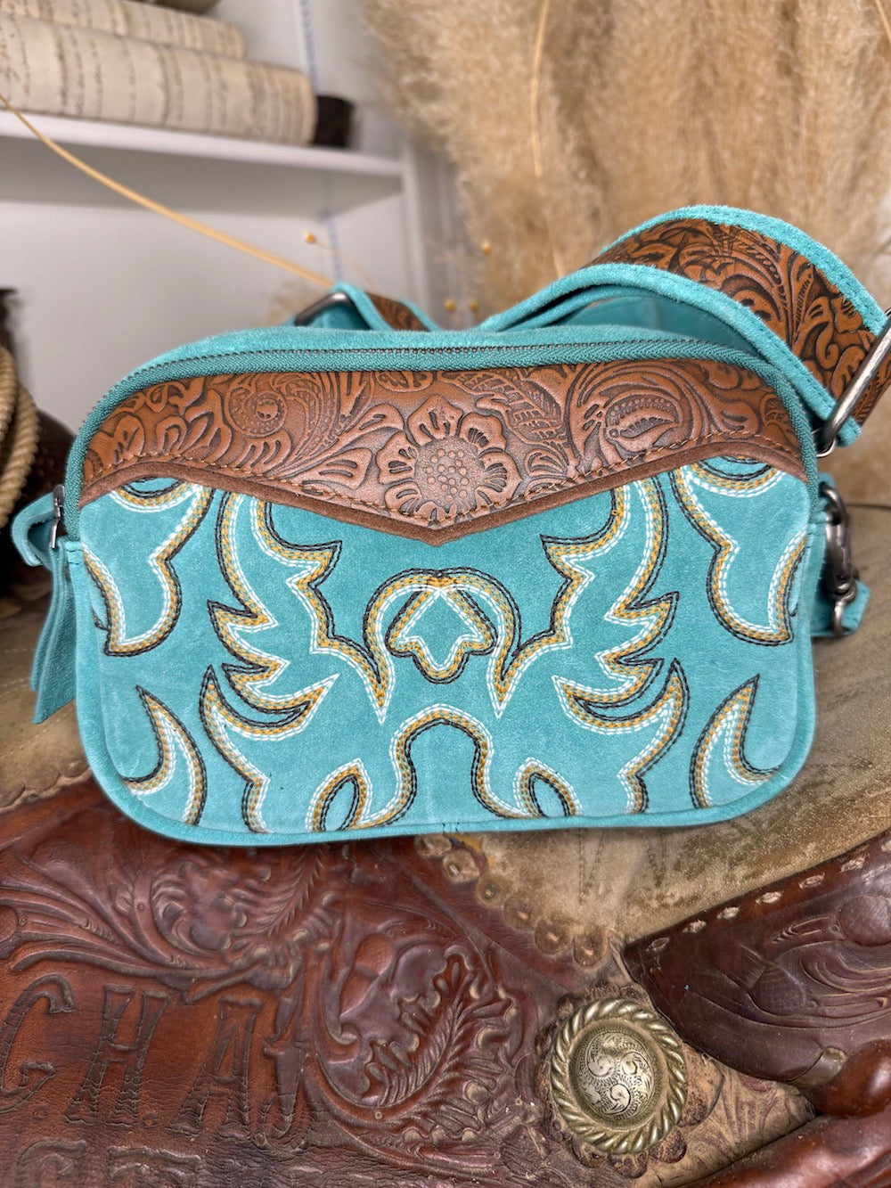 Turquoise suede western crossbody bag with cream and gold boot stitch embroidery and a carved tooled leather rosette