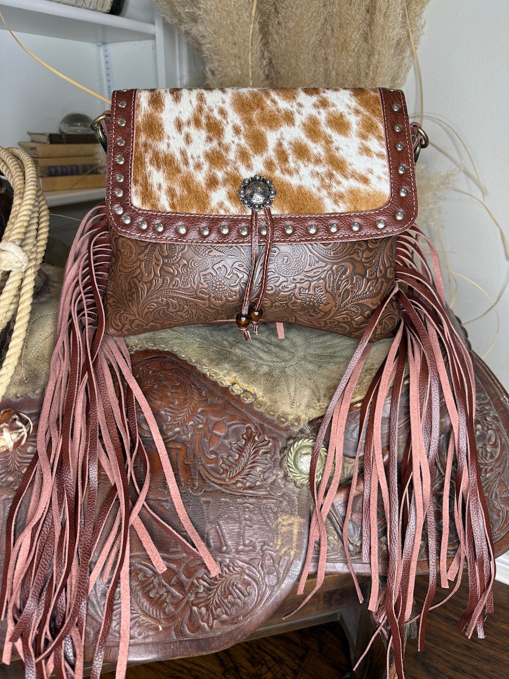 Western shoulder bag with a studded cowhide flap, floral tooled leather body and dusty rose leather fringe