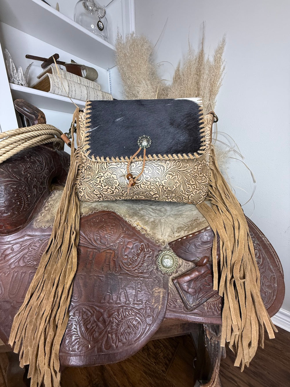Western bag with a black hair-on cowhide flap over champagne gold floral tooled leather, silver concho tassel and tan fringe