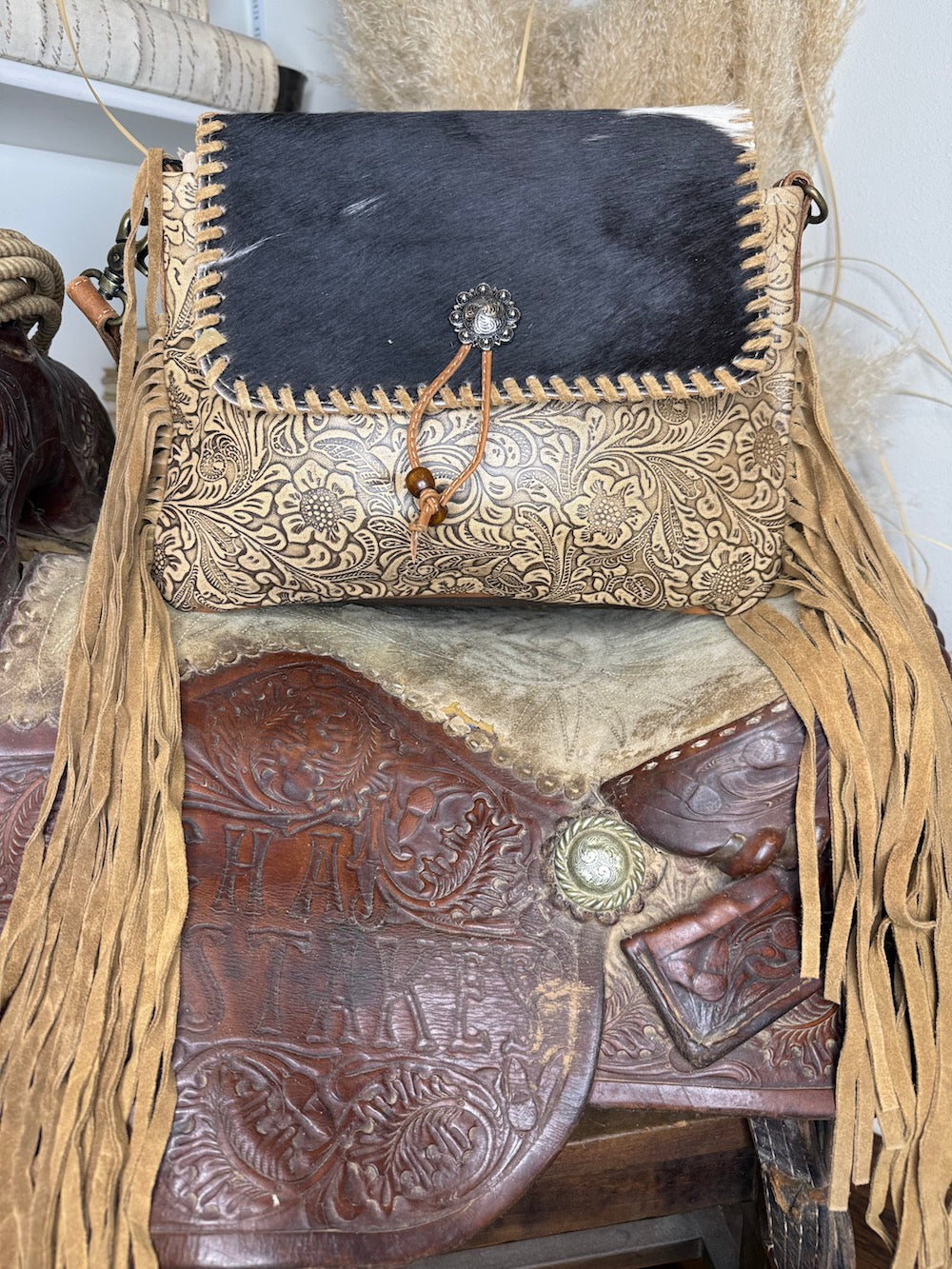 Side view of the black cowhide and gold tooled leather fringe bag showing the whipstitched edge and concho closure