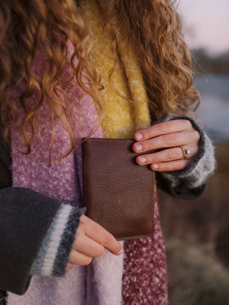 Bison leather passport holder closed, held in hand outdoors at golden hour