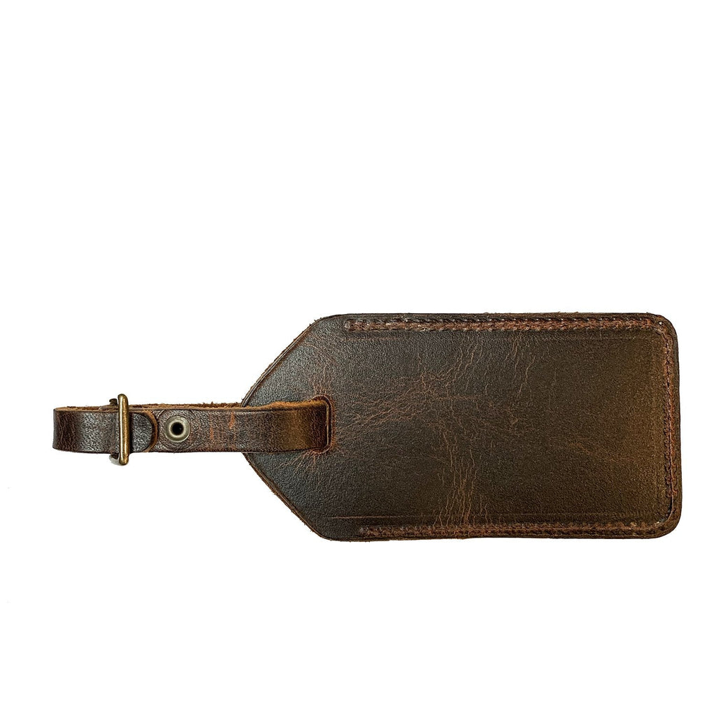 Leather luggage tag flat on white showing the antique bronze buckle and leather strap