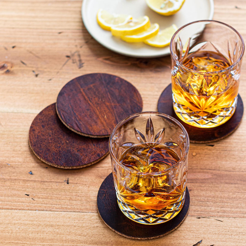 Moose leather coasters with cork backing under two glasses of whiskey on a wood table