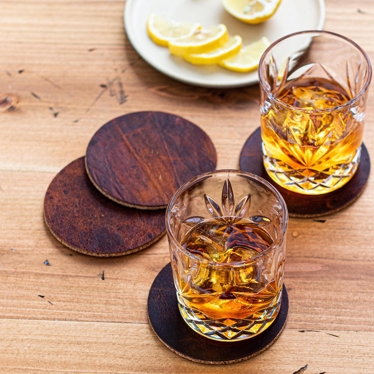 Moose leather coasters with cork backing under two glasses of whiskey on a wood table