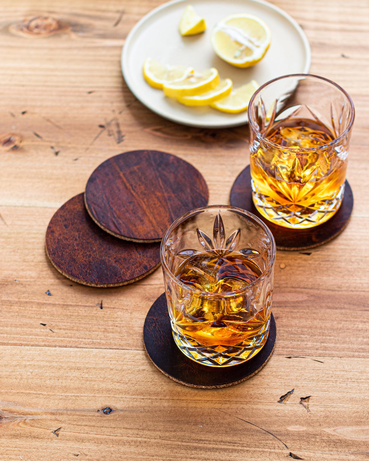 Moose leather coaster set in use with whiskey glasses and sliced lemon on a wood table