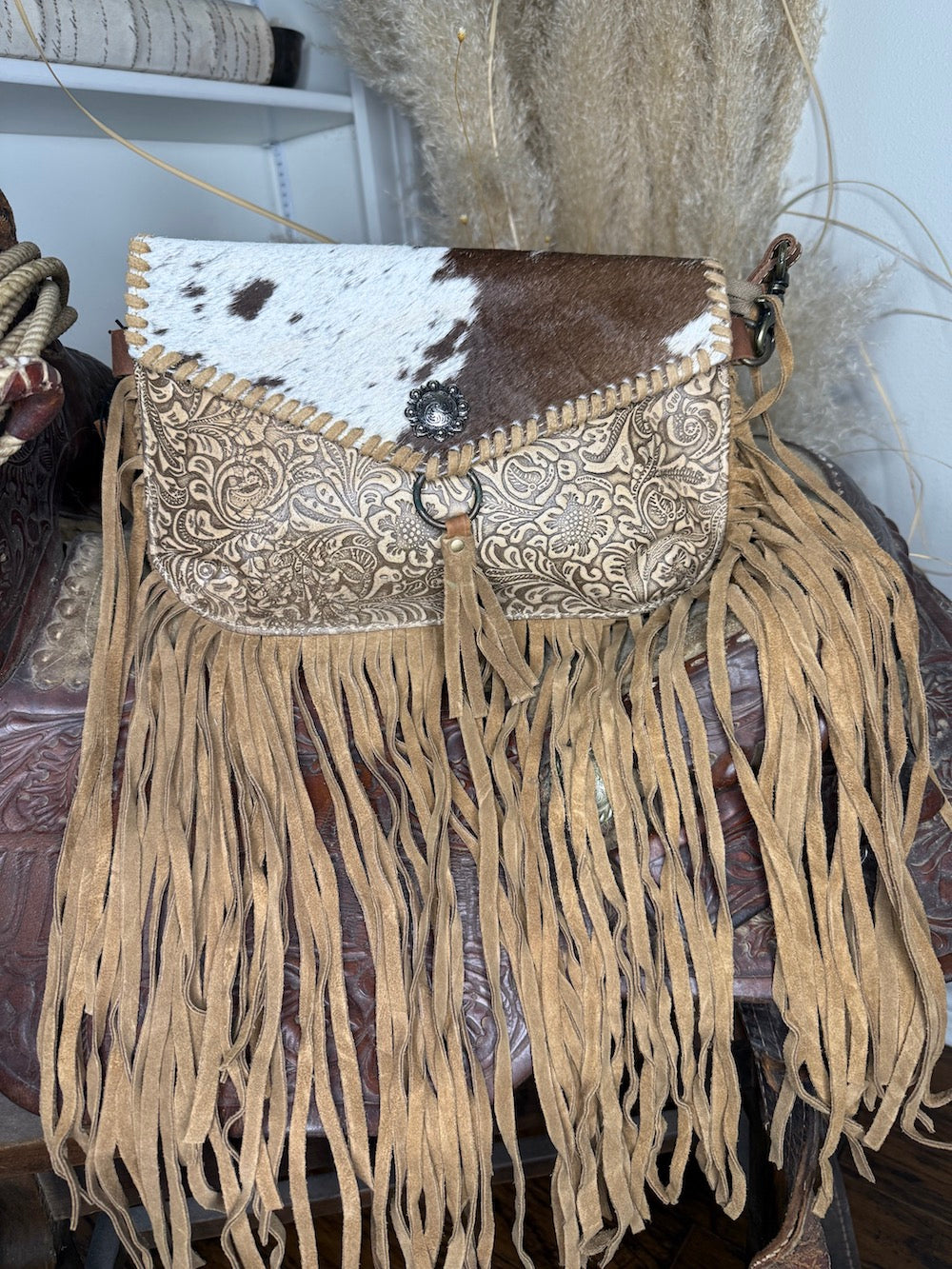 Western crossbody with a brown and white cowhide flap, cream tooled leather body and fringe down the sides and bottom
