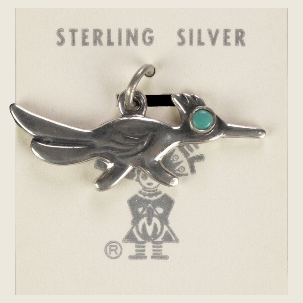 Vintage Maisel's sterling silver roadrunner charm with turquoise eye, shown on a bone linen background