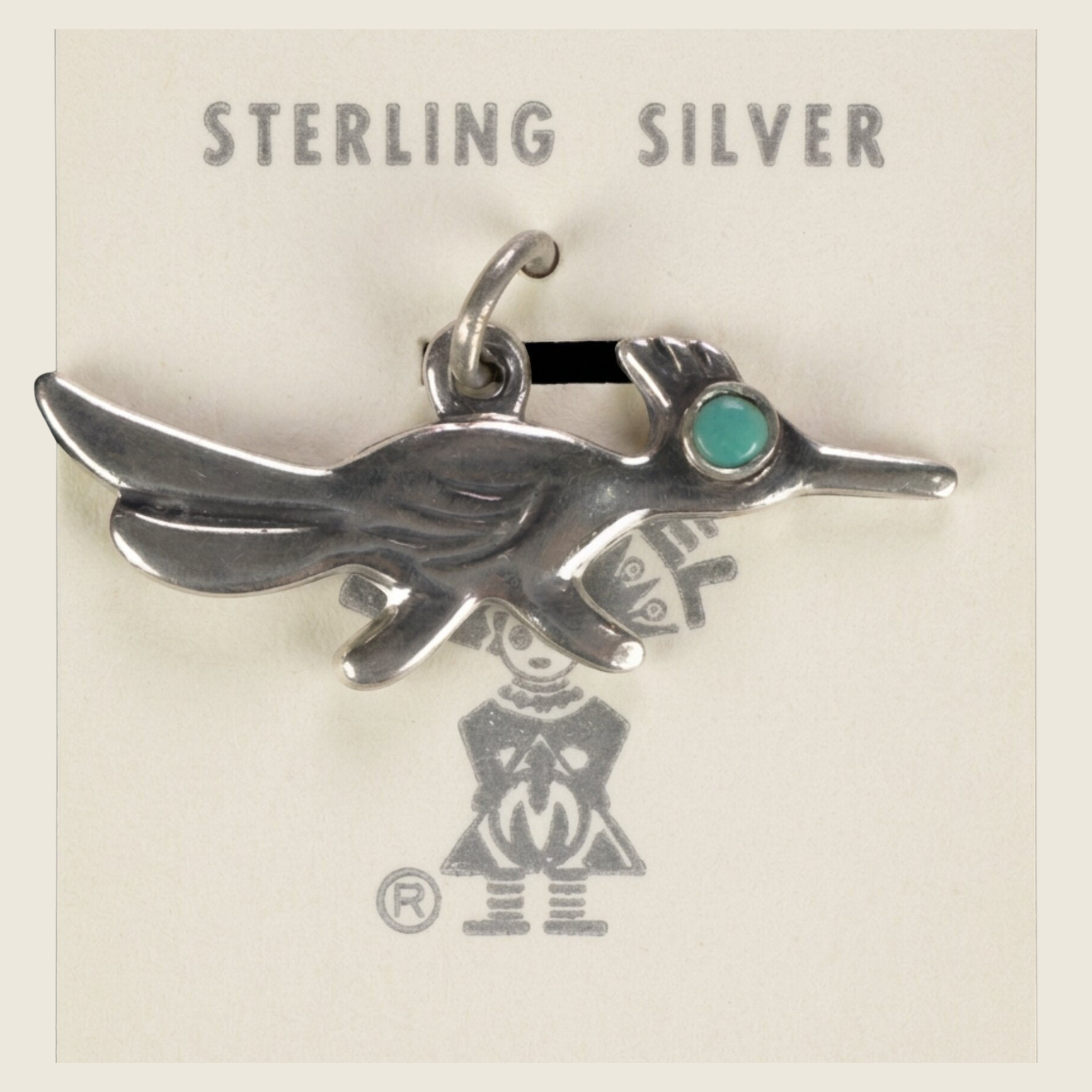 Vintage Maisel's sterling silver roadrunner charm with turquoise eye, shown on a bone linen background