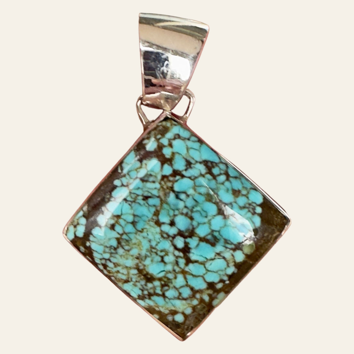Number 8 Spiderweb Turquoise Pendant in Sterling Silver, by Martinez, shown on a cream background