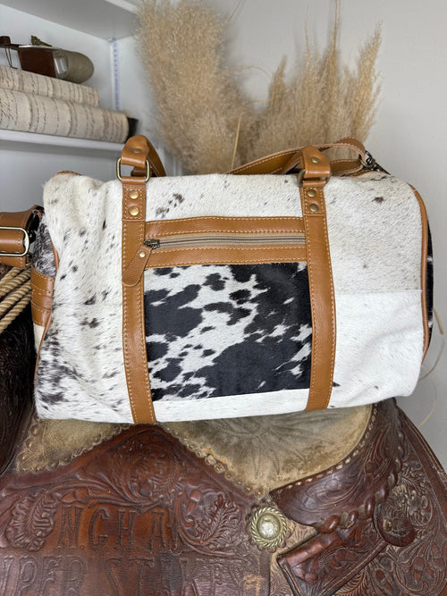 Second view of the patchwork cowhide weekender duffel showing the speckled hide panel and exterior zip pocket