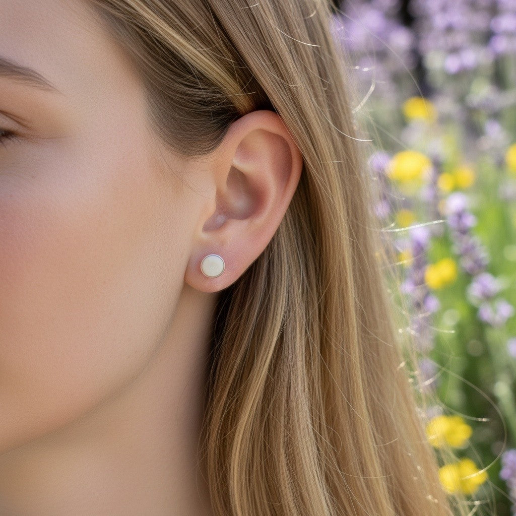 Wildflower Artisans round mother of pearl stud earrings in sterling silver worn by a woman in a garden setting.