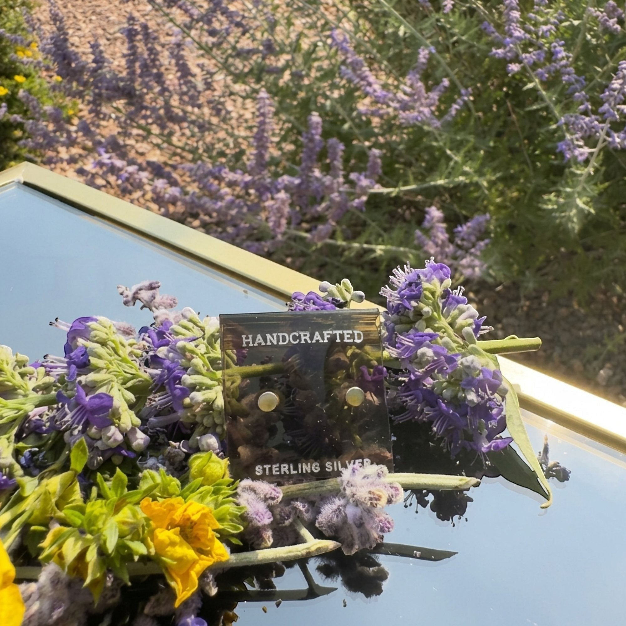 Wildflower Artisans round mother of pearl stud earrings in sterling silver settings displayed with purple flowers.