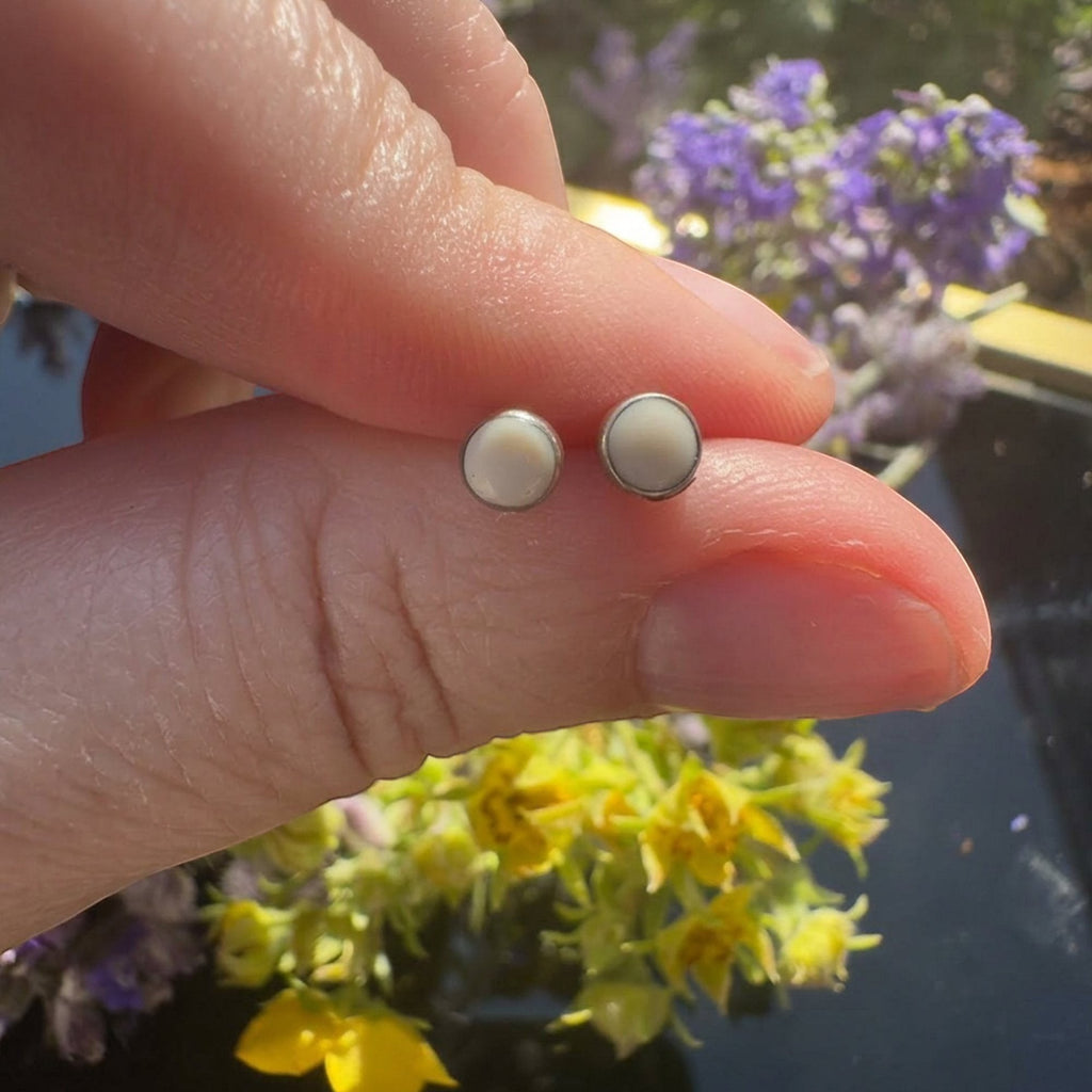 Wildflower Artisans round mother of pearl stud earrings in sterling silver bezels held between fingers.