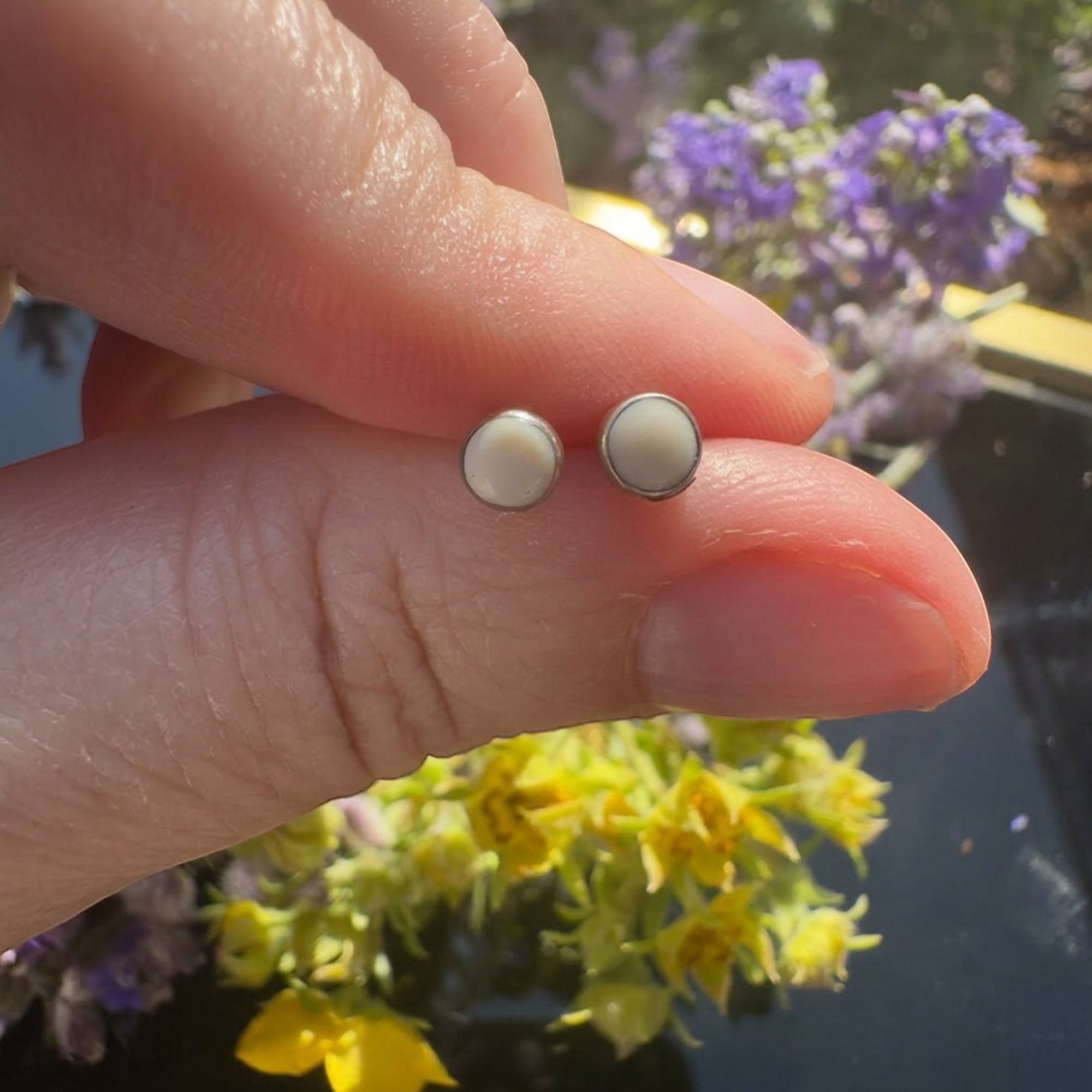 Wildflower Artisans round mother of pearl stud earrings in sterling silver bezels held between fingers.