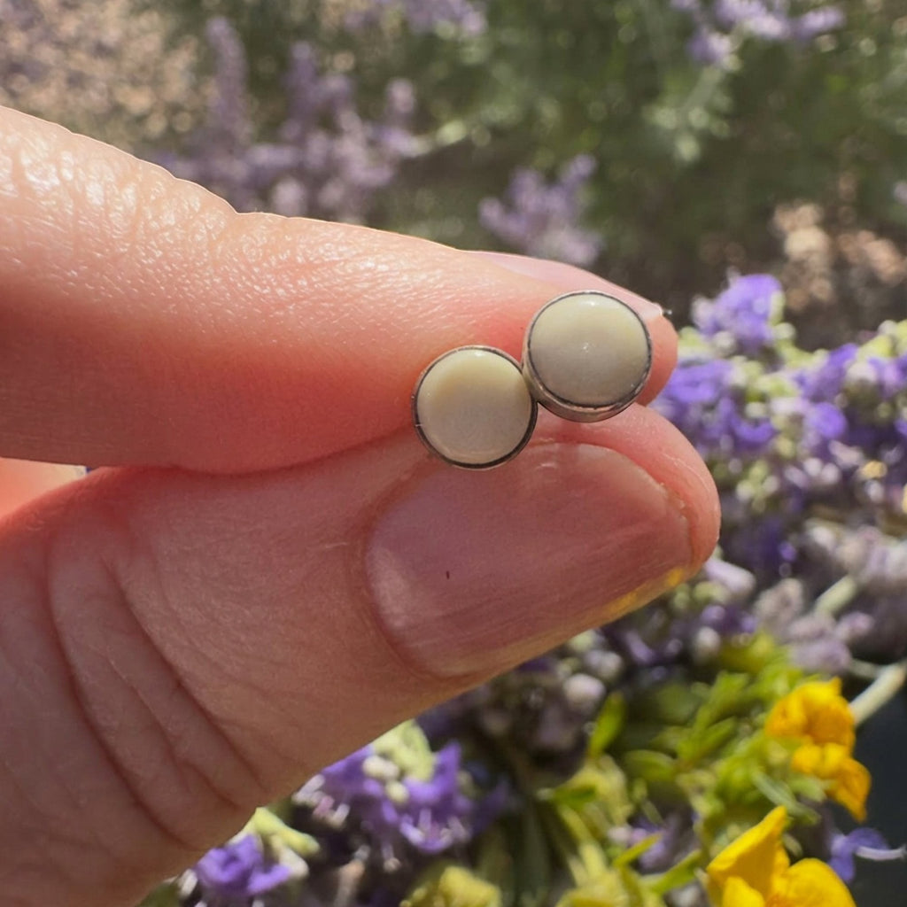 Wildflower Artisans round mother of pearl stud earrings in sterling silver bezels held against a floral background