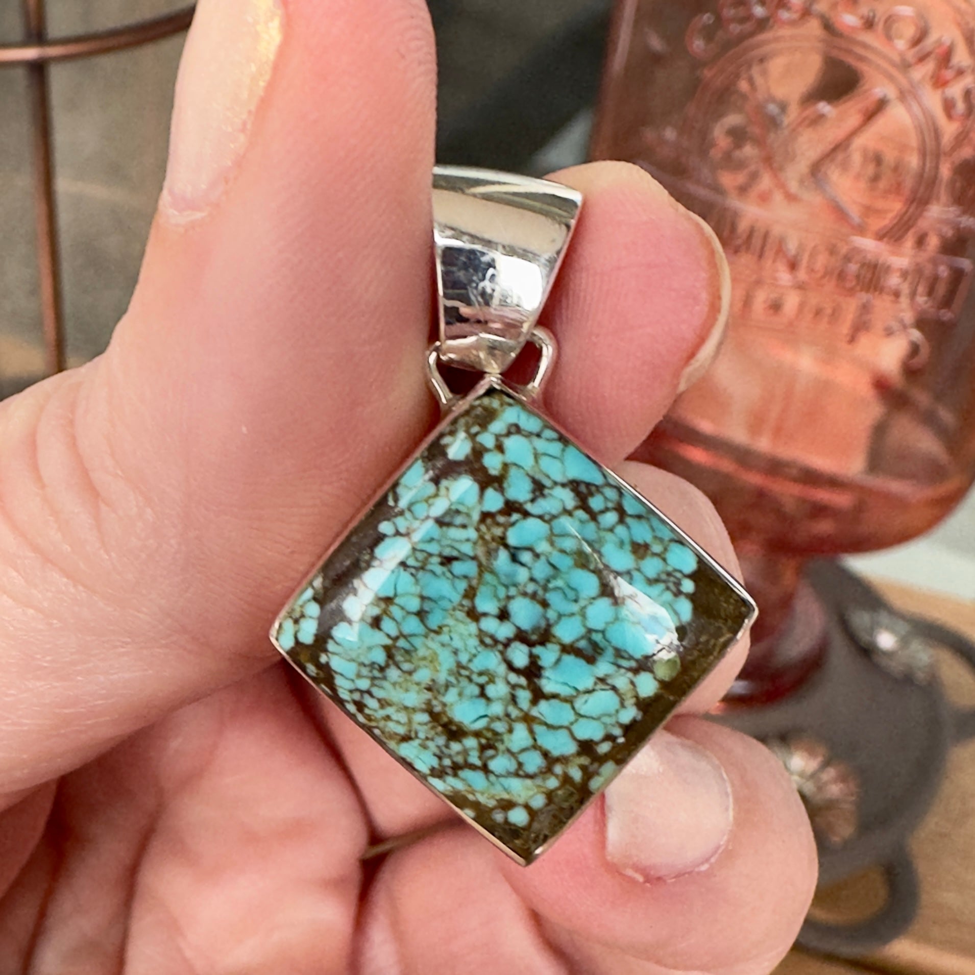 Wildflower Artisans square Number 8 spiderweb turquoise pendant in sterling silver held in hand