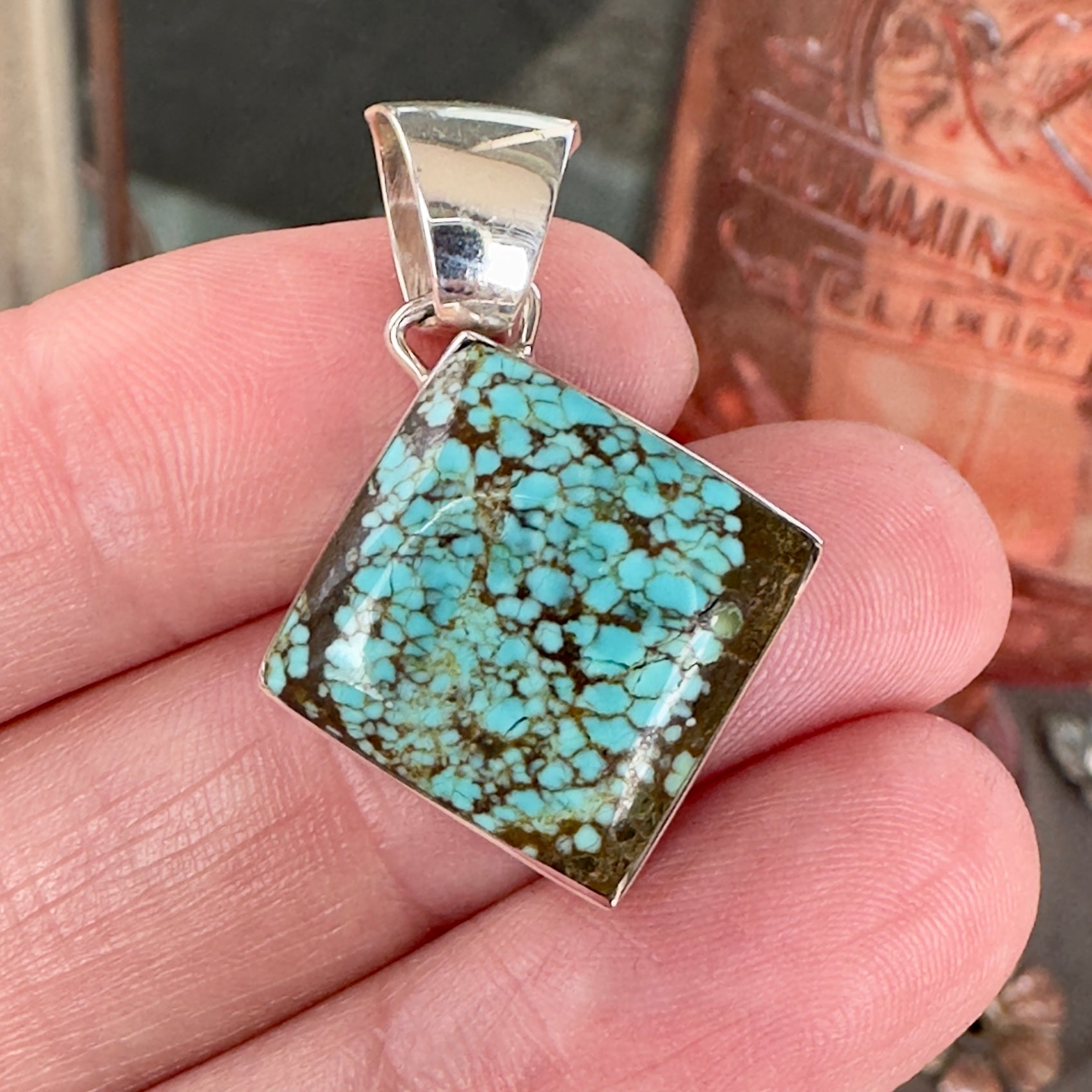 Wildflower Artisans Martinez Number 8 spiderweb turquoise pendant in a square sterling silver setting held in a hand.