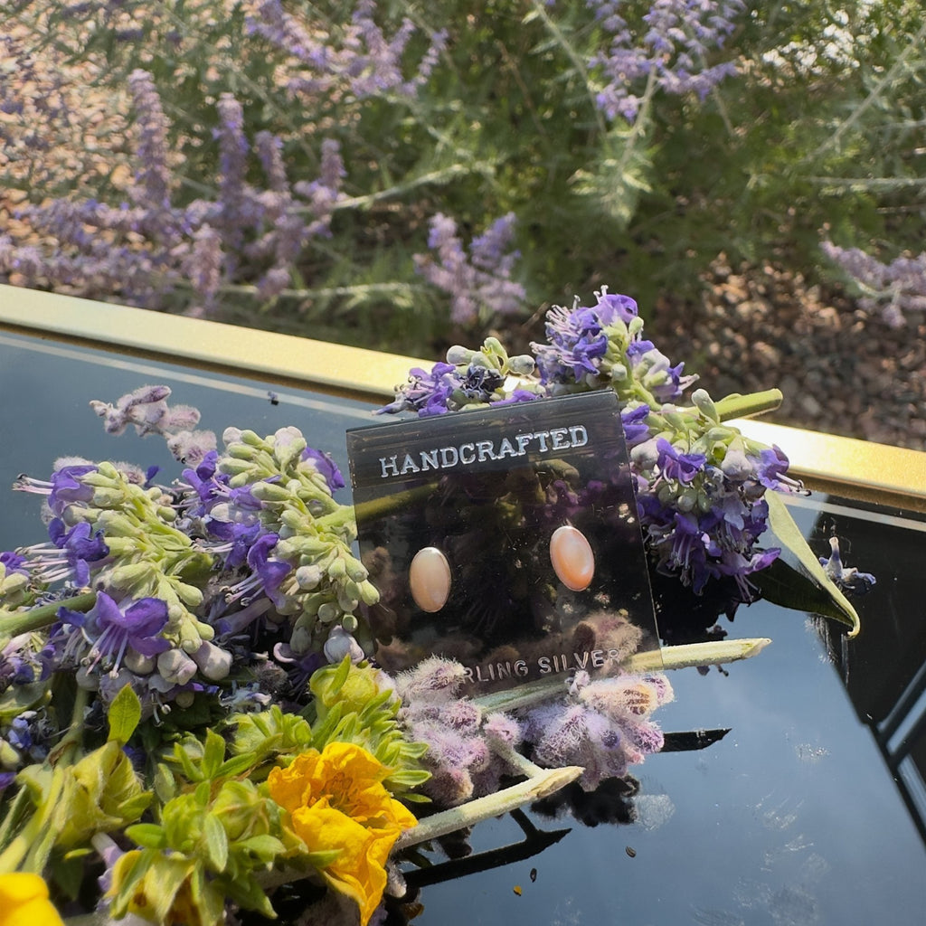 Wildflower Artisans oval opal stud earrings in sterling silver bezels displayed on a card with purple flowers.