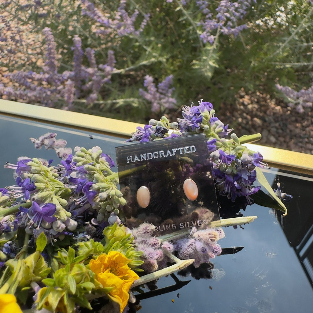Wildflower Artisans oval opal stud earrings in sterling silver settings, displayed on a card with purple flowers.