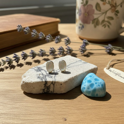 Wildflower Artisans oval opal stud earrings in sterling silver bezels resting on a stone surface.