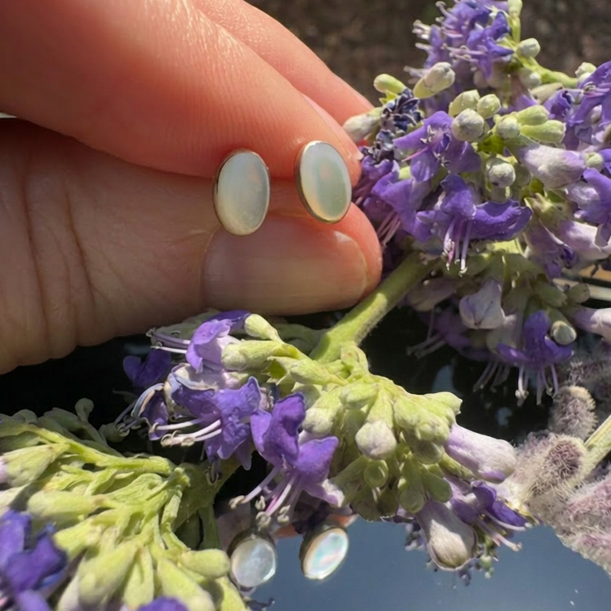 Wildflower Artisans oval opal stud earrings in sterling silver settings held against purple flowers