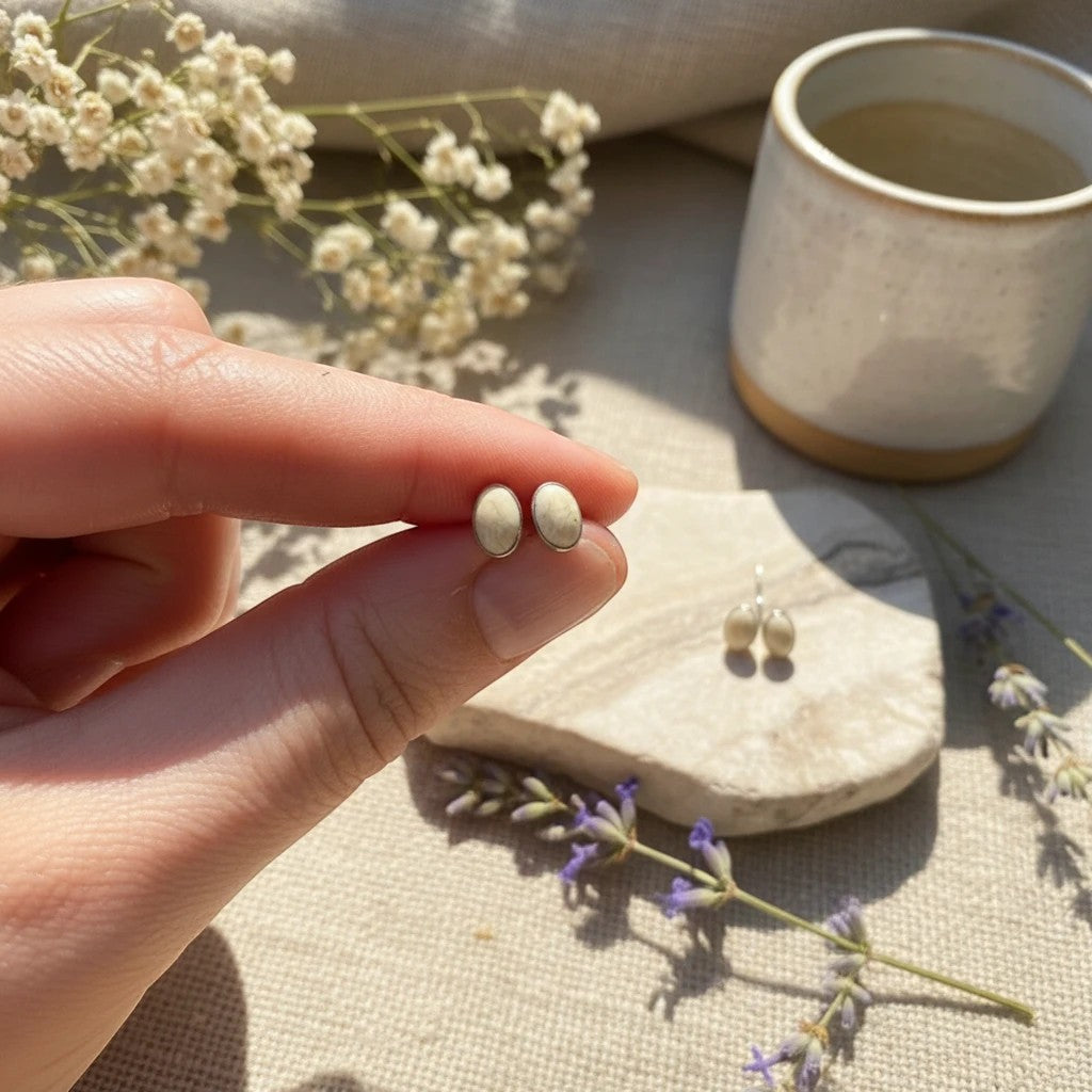 Wildflower Artisans oval stone stud earrings in sterling silver held by fingers with a natural, minimalist aesthetic.