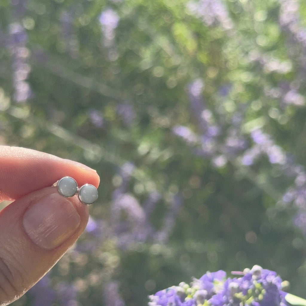 Wildflower Artisans round opal stud earrings in sterling silver bezels held against a blurred floral background