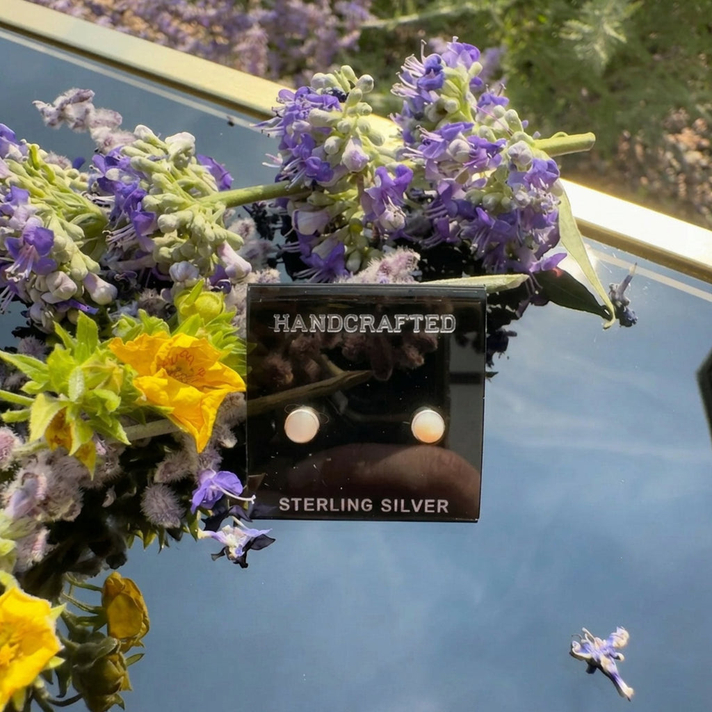 Wildflower Artisans round opal stud earrings set in sterling silver bezels, displayed on a black card with flowers.