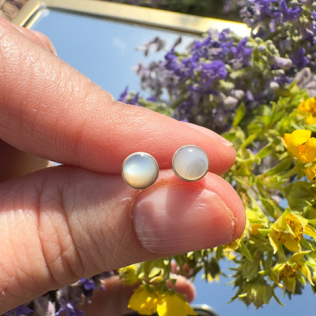 Wildflower Artisans round opal stud earrings in sterling silver bezels held between fingers against a floral background