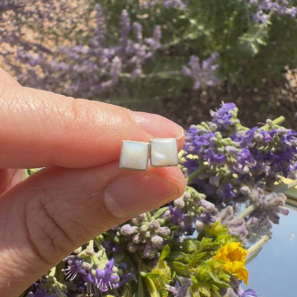 Wildflower Artisans square mother of pearl stud earrings hand-set in sterling silver held against a floral background.