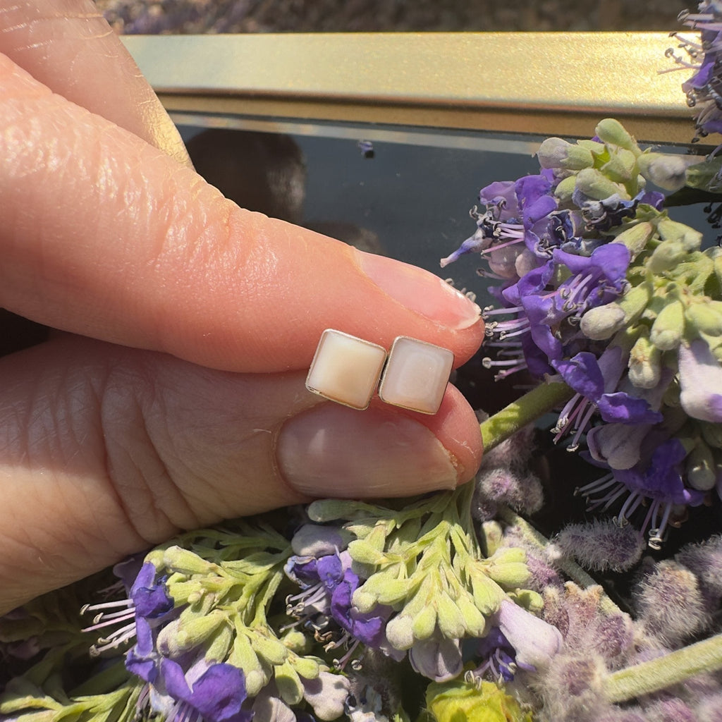 Wildflower Artisans square mother of pearl stud earrings in sterling silver settings held against purple flowers