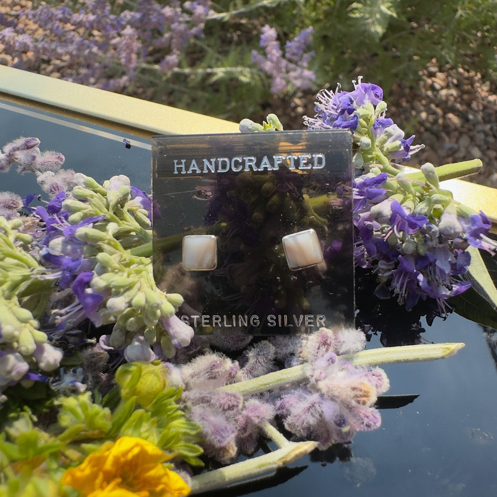 Wildflower Artisans square mother of pearl stud earrings set in sterling silver bezels, displayed with purple flowers.