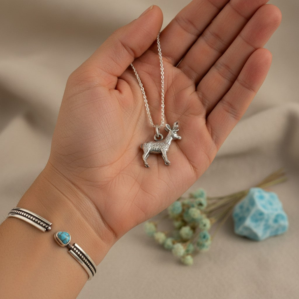 Wildflower Artisans sterling silver standing elk charm necklace held in a hand, featuring a delicate chain.