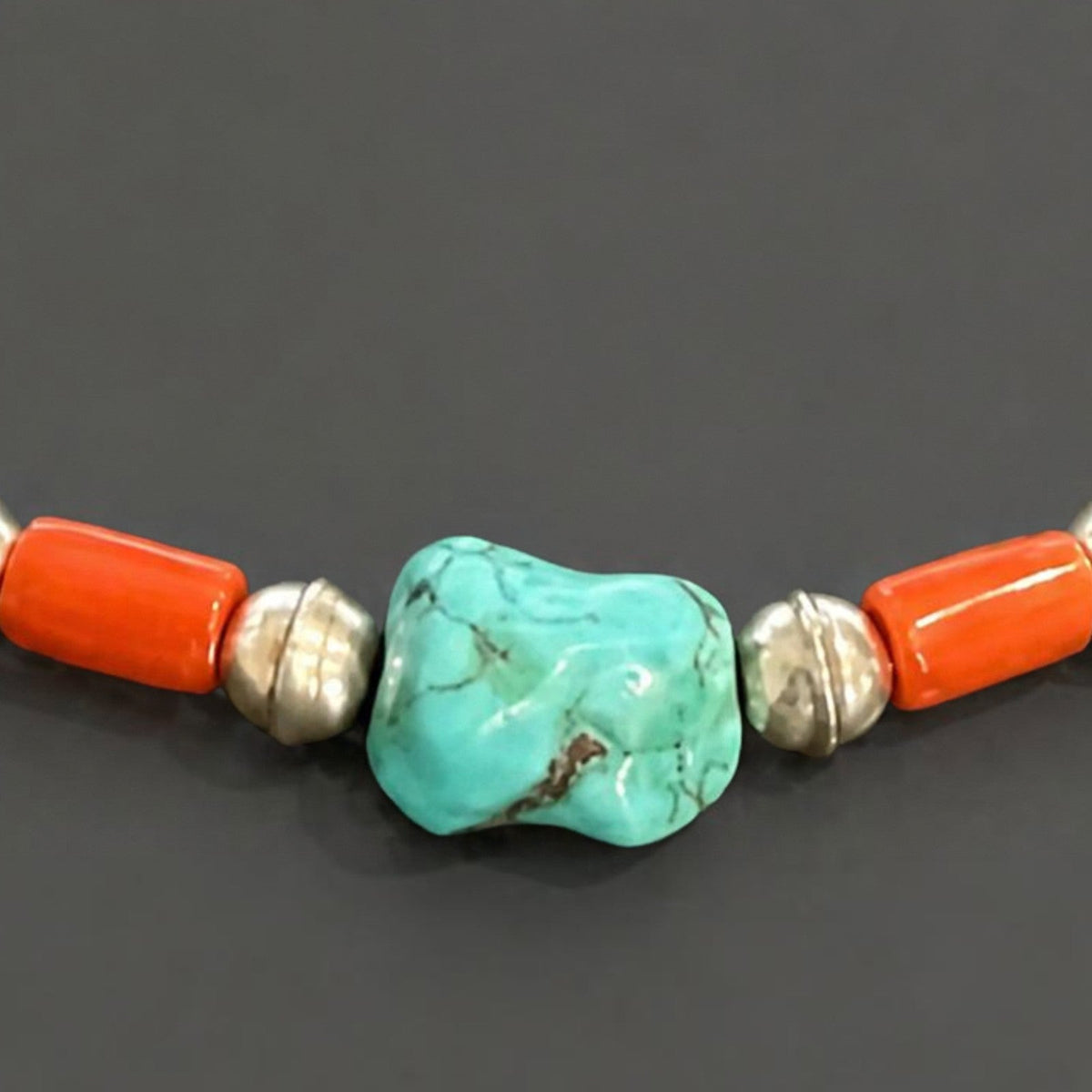 Close-up of the turquoise nugget with brown matrix between red coral barrel beads and sterling silver saucer beads