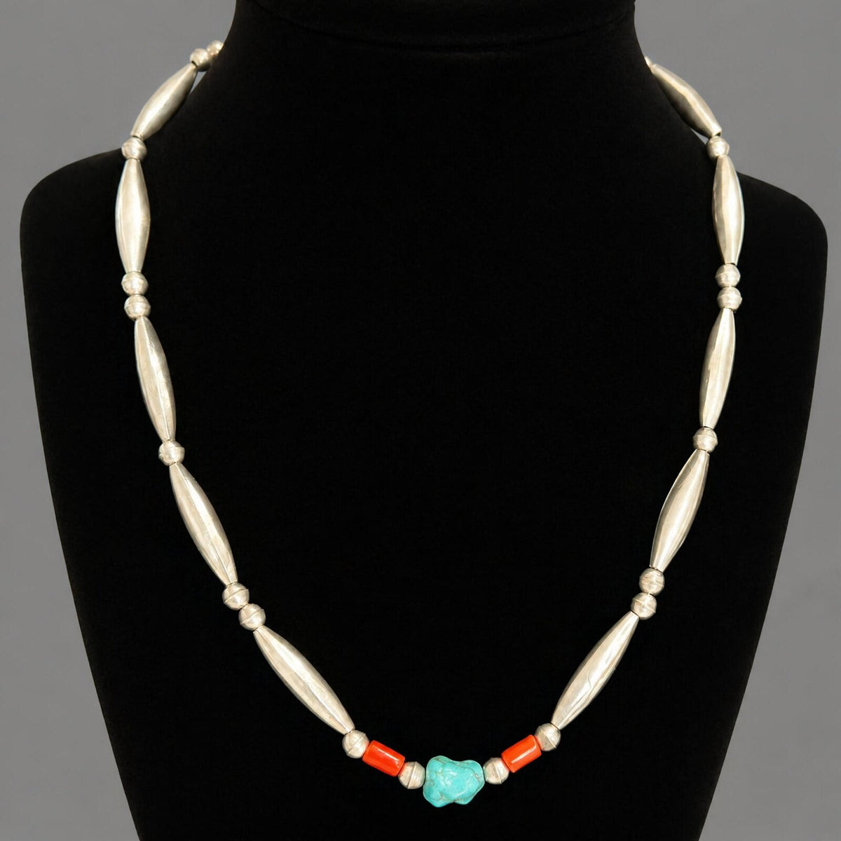 The vintage turquoise and coral necklace on a black velvet bust, sitting at the collarbone